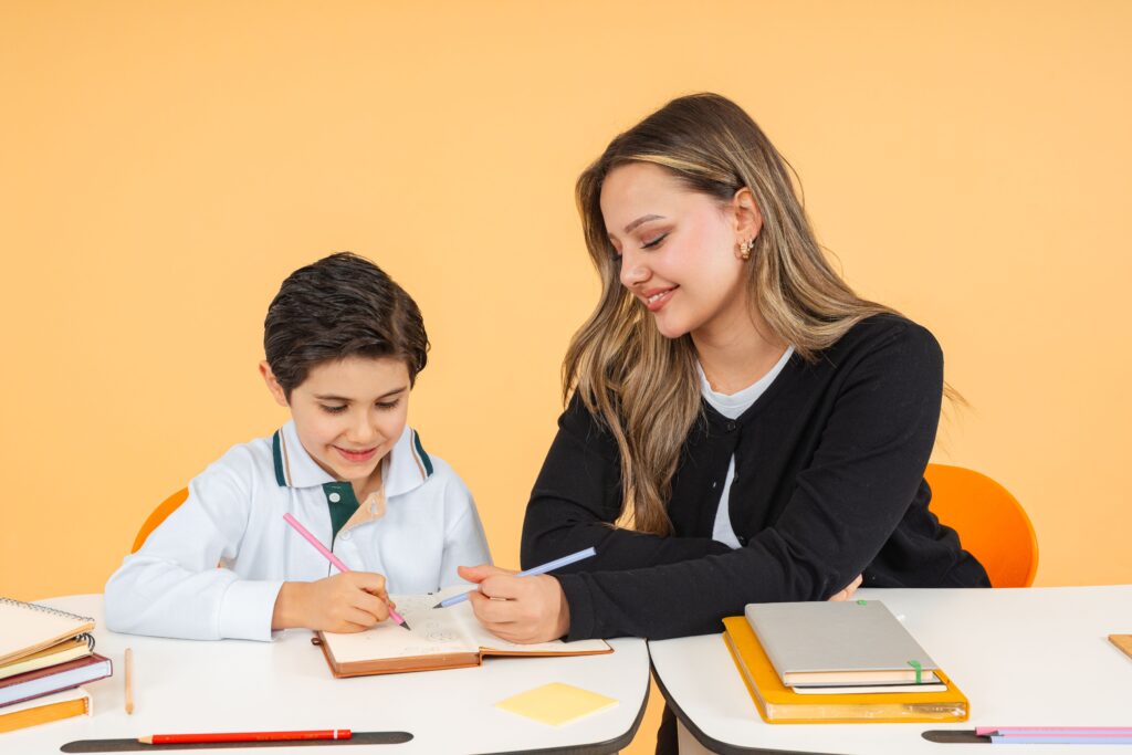 Psychologue scolaire Young teacher helps a schoolboy with writing at a desk, fostering learning.